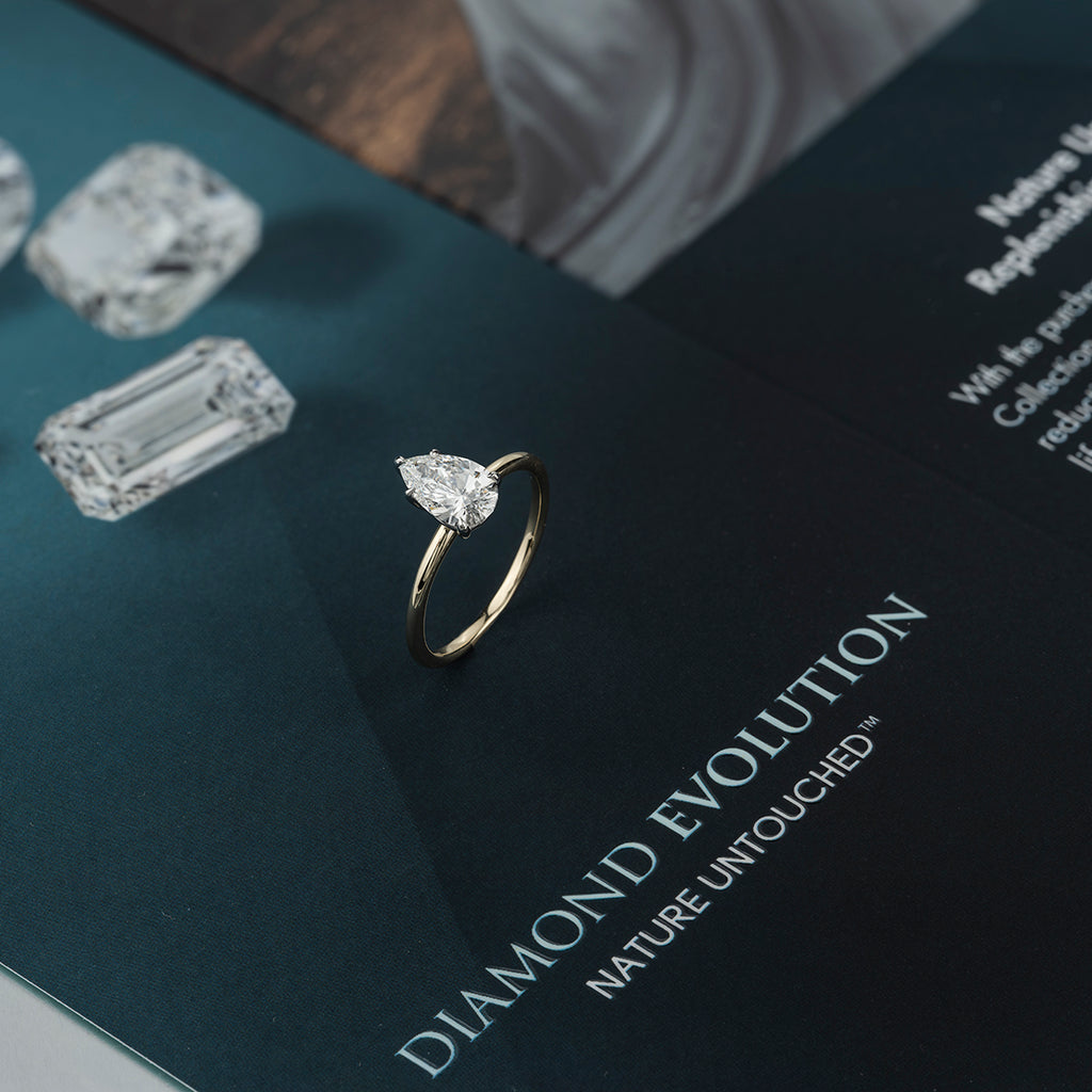A pear cut diamond with white shanks set in yellow gold sitting on top of a diamond evolution certificate. 